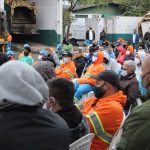 reunião de trabalhadores da comcap com uniformes, roupas de frio e máscaras, a maioria sentada, em pátio da empresa