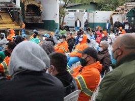 reunião de trabalhadores da comcap com uniformes, roupas de frio e máscaras, a maioria sentada, em pátio da empresa