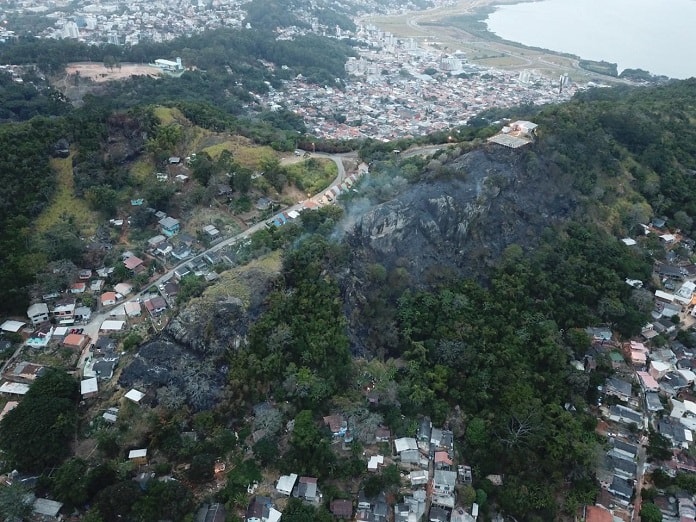 foto aérea mostra topo do morro queimado e casas ao redor