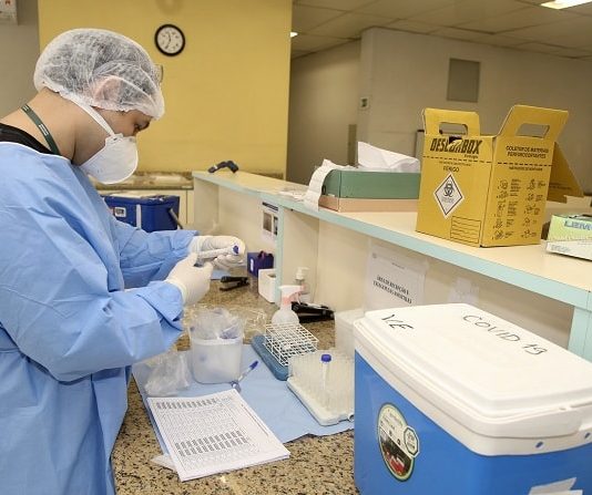 Decreto prorroga estado de calamidade pública até o final do ano em SC profissional de saúde trajado com todos epis manipula instrumentos e amostras sobre balcão em hospital ao lado de caixa térmica