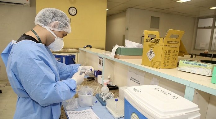 profissional de saúde trajado com todos epis manipula instrumentos e amostras sobre balcão em hospital ao lado de caixa térmica