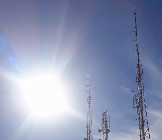 Visando o 5G, IMA lança a licença automática para antenas de telecomunicação diversas antenas vistas à contraluz do sol com equipamentos acoplados e no alto de um morro