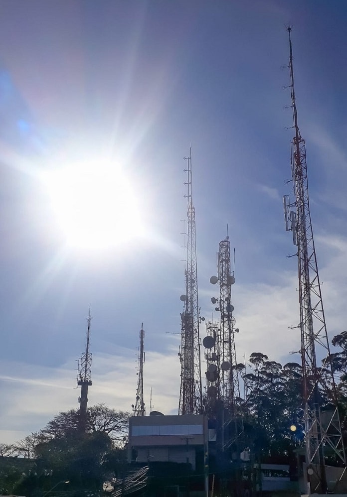 diversas antenas vistas à contraluz do sol com equipamentos acoplados e no alto de um morro