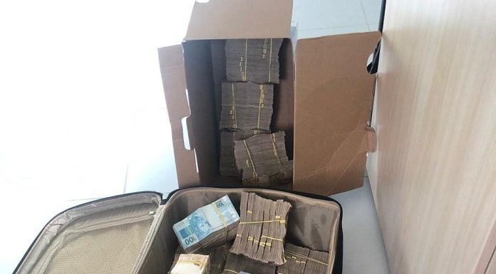 maços de dinheiro presos com elásticos em mala e caixa de papelão no chão de apartamento