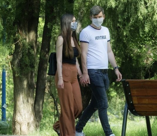 Estado pretende multar quem não usar máscara na rua; veja novas regras em SC homem e mulher brancos, por volta de 30 anos, andam de máscaras e mãos dadas por parque, com banco e árvores ao fundo
