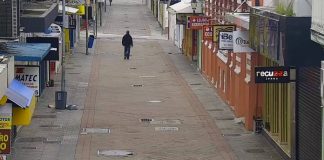 homem usando moletom e calça jeans é visto em imagem de camera de rua andando sozinho em calçadão com comércio em volta fechado no centro de florianópolis