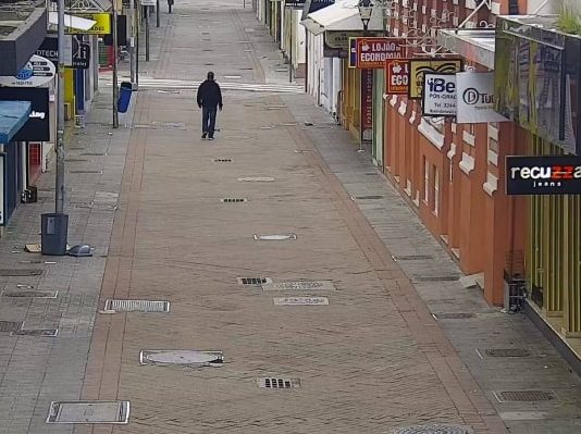homem usando moletom e calça jeans é visto em imagem de camera de rua andando sozinho em calçadão com comércio em volta fechado no centro de florianópolis