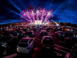 dezenas de carros estacionados em drive-in com show ao fundo