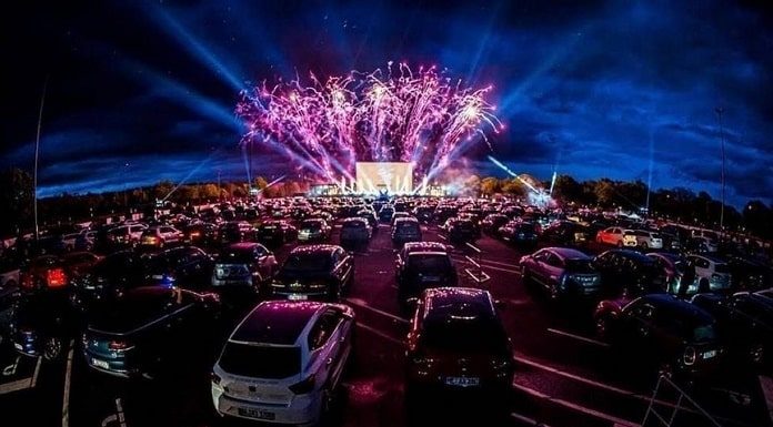 dezenas de carros estacionados em drive-in com show ao fundo