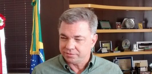 prefeito gean loureiro olha para o lado dentro de seu gabinete, com estante ao fundo com homenagens e bandeiras