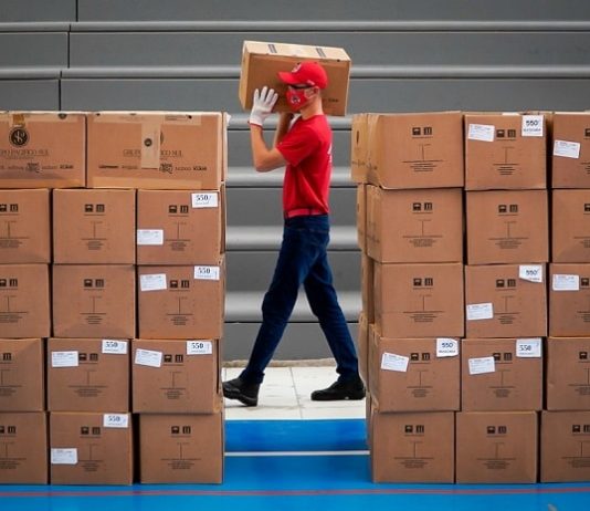 Santa Catarina recebe máscaras de proteção doadas por governo chinês bombeiro voluntário de sc carrega caixa no ombro visto andando no meio de outras pilhas de caixas; ele usa máscara