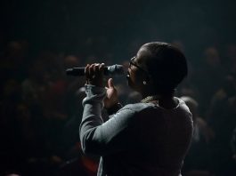 Solicitação de renda emergencial pela Lei Aldir Blanc tem inscrições prorrogadas mulher negra vista de costas cantando segurando microfone em palco