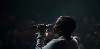 mulher negra vista de costas cantando segurando microfone em palco