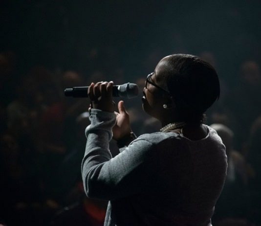 mulher negra vista de costas cantando segurando microfone em palco