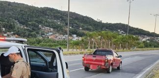 policial mexendo dentro da viatura com porta aberta estacionada atrás do carro gm montana parado no meio da pista direita