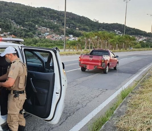 policial mexendo dentro da viatura com porta aberta estacionada atrás do carro gm montana parado no meio da pista direita
