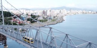 ônibus passando pela ponte hercílio luz vistos em foto aérea com bairro estreito ao fundo