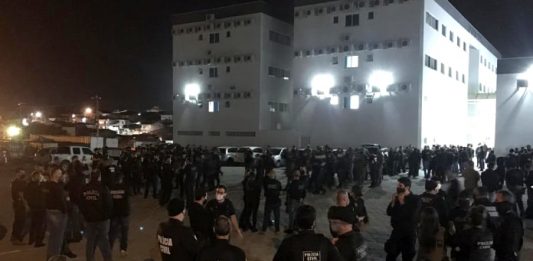 centenas de policias reunidos em pé em pequenos grupos em grande pátio com prédio ao fundo