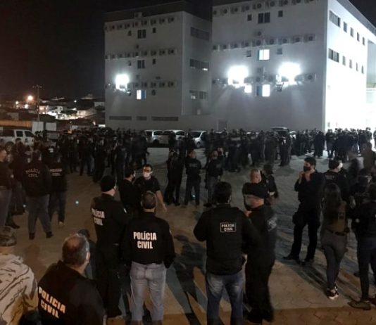 Polícia Civil de SC lança operação Network para prender 83 bandidos do PGC centenas de policias reunidos em pé em pequenos grupos em grande pátio com prédio ao fundo