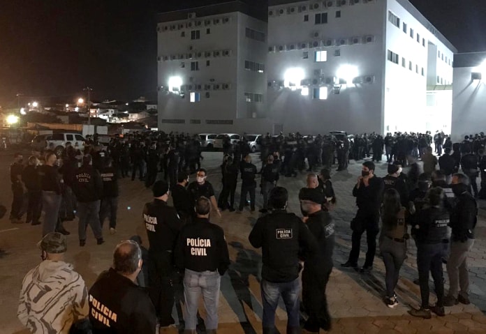 centenas de policias reunidos em pé em pequenos grupos em grande pátio com prédio ao fundo