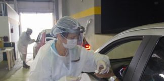 profissional de saúde usando equipamentos de segurança coleta amostra de sangue de dedo de homem com mão para fora do carro dentro de ginásio