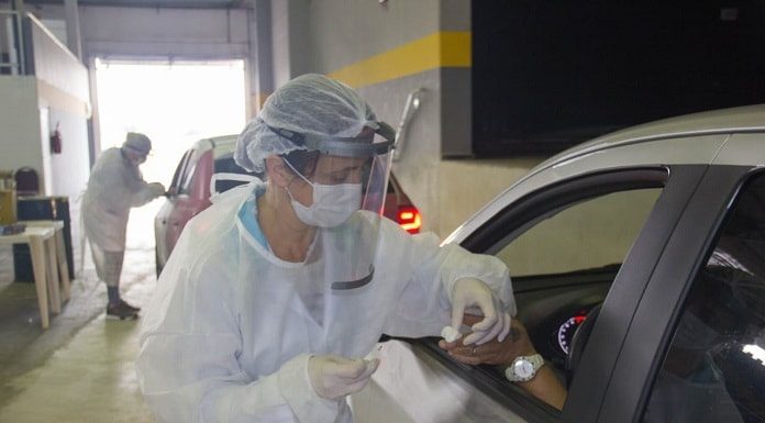 profissional de saúde usando equipamentos de segurança coleta amostra de sangue de dedo de homem com mão para fora do carro dentro de ginásio