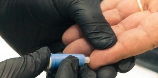 pessoas usando luva preta retira amostra do dedo de outra pessoa branca