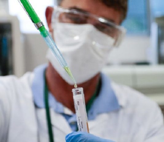 Homem vestindo jaleco branco segurando u frasco na mão