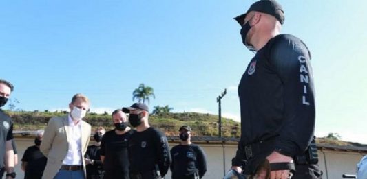 Concurso público para contratação de agentes penitenciários será retomado em julho homens de pé usando máscaras e policial segurando um cachorro