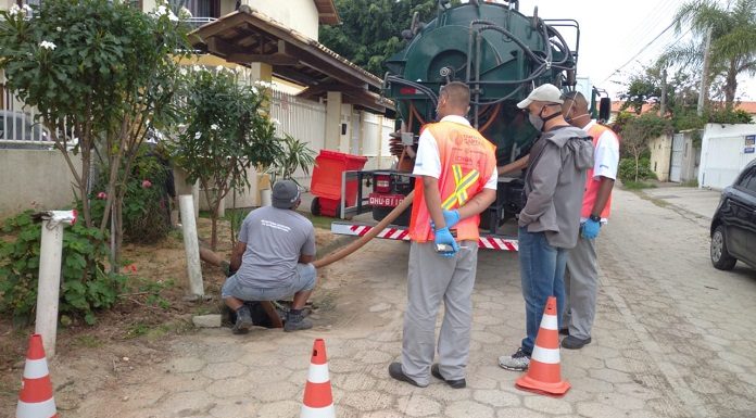 1 homem agachado e três homens em pé, verificando a rede de esgoto