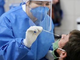 mulher vestindo jaleco azul, com luvas brancas fazendo o teste em homem usando máscara verde