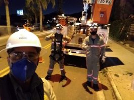 funcionário da celesc usando epi faz selfie com dois colegas posando atrás ao lado do caminhão