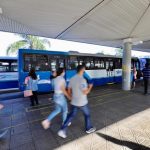 pessoas correndo em plataforma do ticen com ônbus estacionados em volta