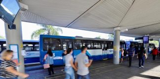 pessoas correndo em plataforma do ticen com ônbus estacionados em volta