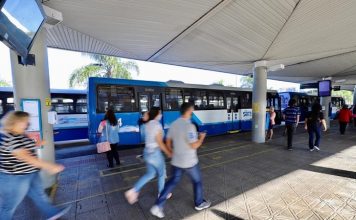 pessoas correndo em plataforma do ticen com ônbus estacionados em volta
