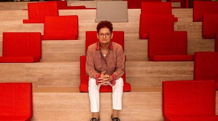 margareh sentanda em poltrona vermelha de auditório com as mãos cruzadas para frente olha para a câmera