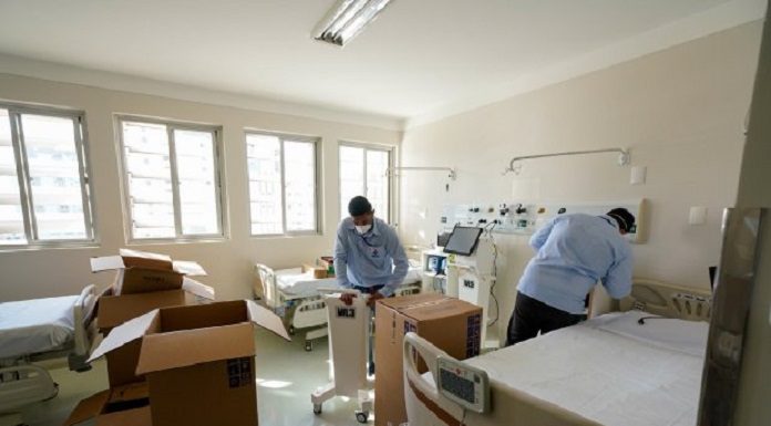 dois homens desencaixotam equipamentos dentro de quarto de enfermaria com duas camas