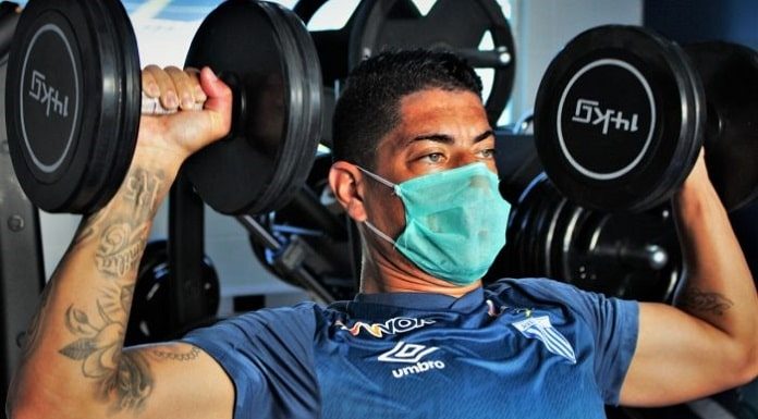 homem de camiseta azul, usando máscara fazendo exercícios em academia