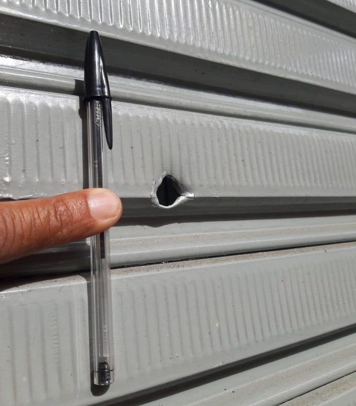 buraco de bala em porta de metal com uma caneta bic segurada ao lado para medir