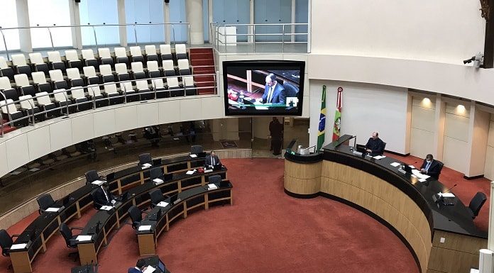 plenário da alesc praticamente vazio, com schuster em trasmissão no telã