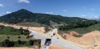 foto aérea de pequeno túnel em construção com morros ao fundo e caminhões por perto