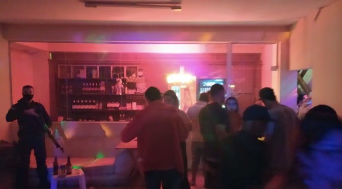 Guarda de São José flagra 50 pessoas em pé em ambiente pouco iluminado da boate, em frente ao balcão do bar; ao lado policial com escopeta