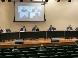 Relatório final da CPI dos Respiradores será apresentado em 20 de agosto deputados membros da cpi sentados ao longo de bancada sobre palco de auditório com telão acima
