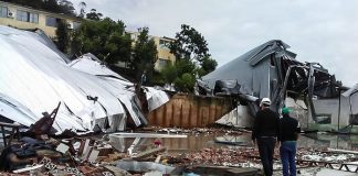 estrutura desabada repleta de escombros pelo chão; dois homens com capacete no meio dos estragos