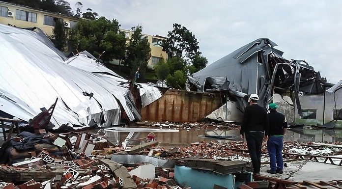 estrutura desabada repleta de escombros pelo chão; dois homens com capacete no meio dos estragos