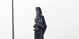 estátua de são josé usando máscara; é a estatua que fica na av. beira mar e mostra são josé segurando menino jesus; morro da cruz ao fundo