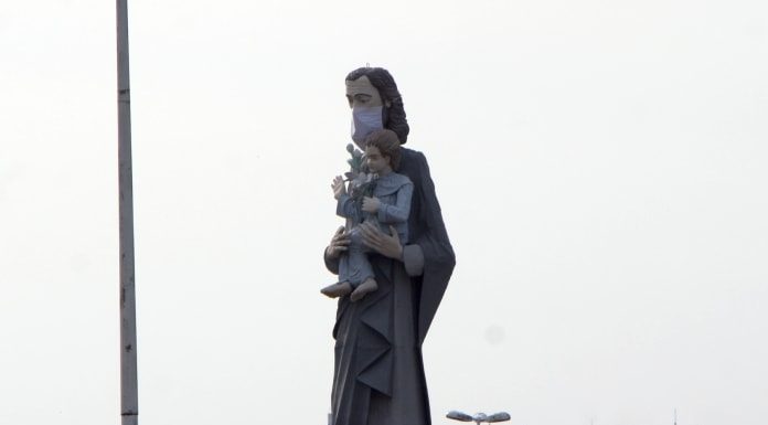 estátua de são josé usando máscara; é a estatua que fica na av. beira mar e mostra são josé segurando menino jesus; morro da cruz ao fundo