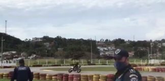 na pista do kartódromo agente faz sina de parada e outro anda em direção às barricadas de pneus; moto passando na curva