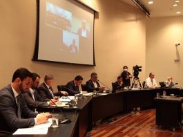 Membros da CPI afirmam que há inconsistências em respostas do governador sobre respiradores parlamentares sentados ao longo de bancada em palco com telão acima