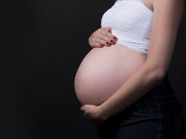 mulher grávida vista de lado com barriga de fora e com as mãos em cima e embaixo